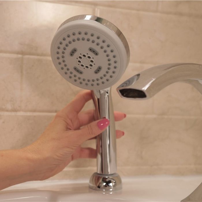 Chrome handheld shower head held beside a curved bath spout