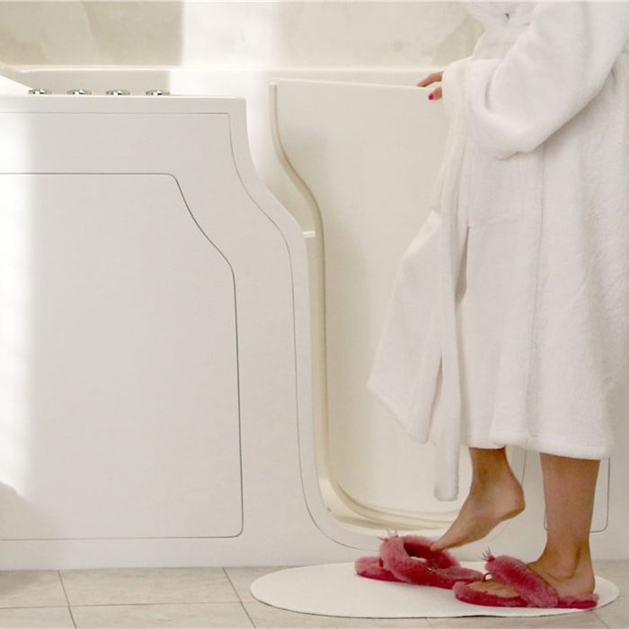 Person in a robe stepping through the open door of a walk-in bathtub